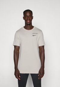 Camiseta de algodón gris claro con cuello redondo y mangas cortas; presenta un logo negro "SPURS" y un swoosh de Nike en el pecho.