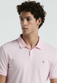 Lichtroze polo shirt met een kraag, twee knopen en een klein geborduurd pinguïnlogo op de linkerkant van de borst. Gladde stofstructuur.