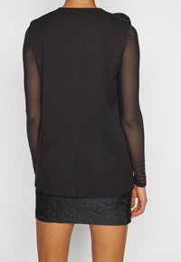 Černý top s průhlednými dlouhými rukávy, texturovaná látka a volný střih; spárovaný s krátkou texturovanou černou sukní s květinovým vzorem.