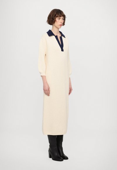 Rochie tricotată crem cu guler bleumarin și jumătate de placket, mâneci lungi, croi drept, țesătură texturată, asortată cu cizme negre până la genunchi.