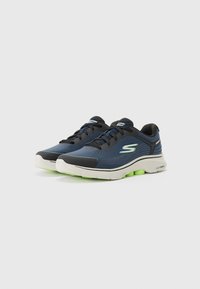 Blaue und schwarze Sportschuhe mit einer strukturierten Oberseite, weißer Sohle und grünen Akzenten, ausgestattet mit einer Schnürung und Logodetails.
