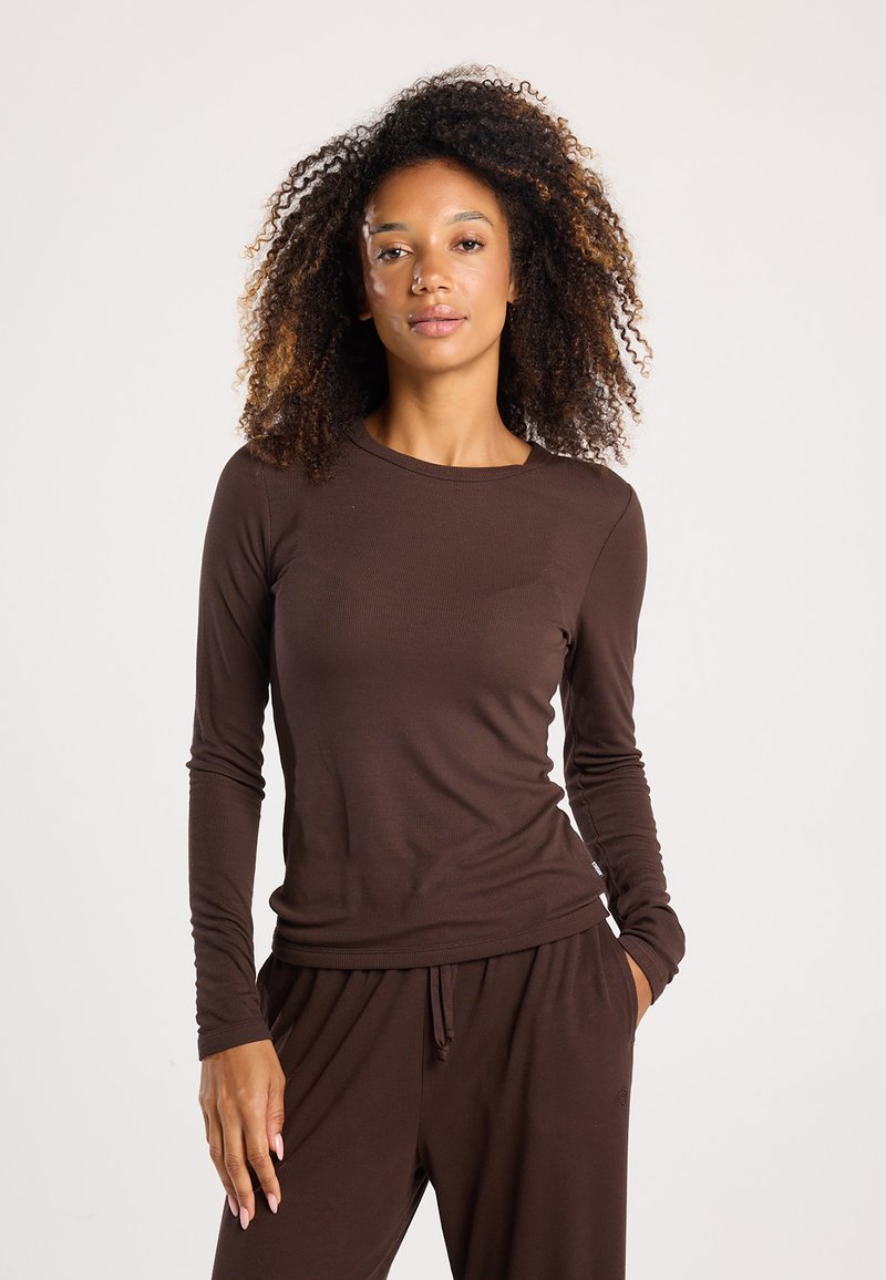 Brown long-sleeve top with a round neck, ribbed texture, and fitted design. Worn with matching brown pants, featuring an elastic waistband.