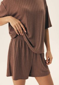 Brązowy dres z prążkowaniem, składający się z luźnej bluzki z krótkimi rękawami i spodenek z elastycznym paskiem. Miękka tekstura i casualowy design.