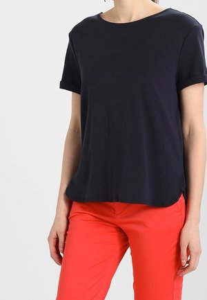 Camiseta de manga corta azul marino con escote redondo, con un dobladillo trasero ligeramente más largo, combinada con pantalones ajustados rojos brillantes.