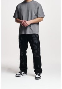 T-shirt gris en coton à coupe décontractée, associé à un jean en denim noir déchiré avec des patches texturés, complété par des baskets noires et blanches.