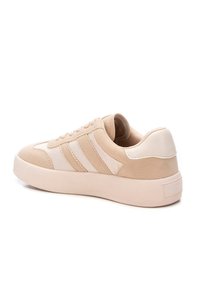 Zapatilla beige con parte superior de cuero liso y acentos de ante, que presenta tres franjas texturizadas, punta redondeada y una suela gruesa.
