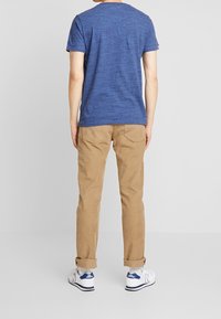 Niebieska teksturowana koszulka z krótkim rękawem, beżowe spodnie z podwiniętymi nogawkami i białe trampki z niebieskimi akcentami, widok z tyłu.