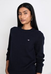 Maglione a maglia blu navy con collo rotondo e polsini a coste, caratterizzato da un piccolo logo sul petto. Tessuto morbido e vestibilità classica.
