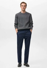 Pulover gri tricotat cu textură canelată, purtat cu pantaloni în dungi bleumarin închis. Pantofi negri completează look-ul.