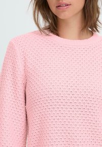 Hellrosaner Strickpullover mit strukturiertem Muster, rundem Ausschnitt und gerafften Bündchen. Das Material wirkt weich und atmungsaktiv.