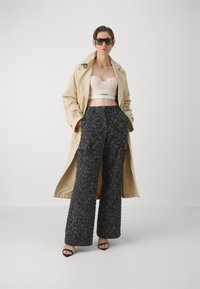 Beige trenchcoat over en nude strukturert crop top og svarte teksturerte vide bukser med lommer. Slanke svarte hælsandaler fullfører antrekket.