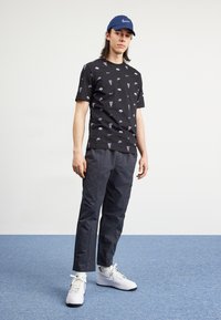 Black cotton t-shirt with small white Nike logos and text, paired with dark gray trousers and white Nike sneakers with black accents.