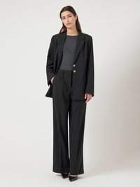 Μαύρο κοστούμι ραμμένο με διπλό πέτο και χρυσά κουμπιά, συνοδευόμενο από παντελόνι με φαρδιά μάτια. Λείο ύφασμα με δομημένη εφαρμογή. Μαύρες γόβες.