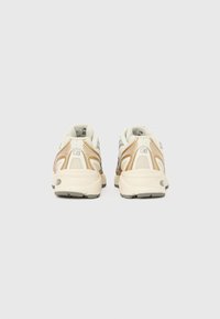 Ténis de corrida com parte superior creme, detalhes em cinza e pormenores em laranja. Possuem uma sola acolchoada e material em malha para respirabilidade.