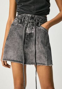 Denim skirt in black and gray gradient, featuring a tie belt, front pockets, and frayed hem. Textured fabric with visible seams.