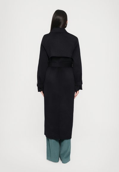 Abrigo largo negro con cuello alto, cintura ajustada y diseño de espalda abierta. Tiene mangas largas y una textura elegante y suave.