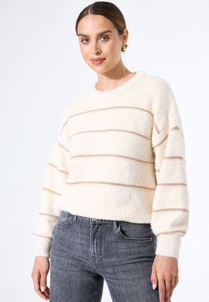 Pull crème avec des rayures beige horizontales, texture douce, encolure ronde et manches amples, associé à un jean gris foncé.