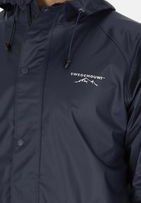 Marine vandtæt jakke med hætte, prydet med et hvidt logo "SWEDEMOUNT", trykknaplukninger og snoretræk detaljer til justerbar pasform.