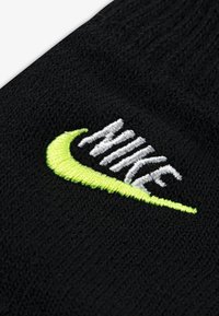 Černá pletenina s výrazným bílým logem "NIKE" a zeleným akcentujícím swooshem na spodní části. Měkká textura s hustým tkaním.