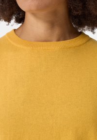 Maglione giallo a maglia con scollatura rotonda a costine. Texture liscia con una finitura uniforme e un colore omogeneo in tutto il capo.
