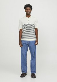 Polo shirt i lys beige med marineblå vandrette striber, korte ærmer og en to-knaps knaplukning, parret med lyseblå afslappede jeans.