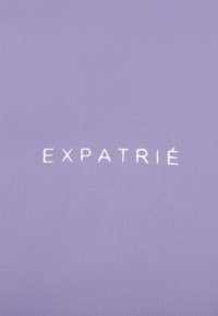 Purple textured surface featuring the word "EXPATRIÉ" in white embossed lettering, showcasing a minimalist design and smooth finish.