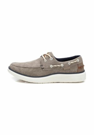 Zapato de lona gris claro con punta redonda, suela de goma blanca, forro azul marino y acentos en tonos marrones. Presenta dos ojales y detalles de costura en contraste.
