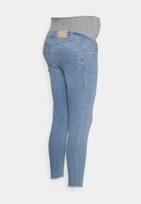 Jeans de denim azul claro com uma cintura elástica cinza. Fit slim, com bolsos traseiros e uma bainha com acabamento desfiado. Patch de couro na cintura traseira.