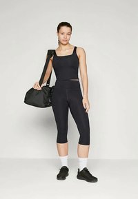 Crni sportski crop top i leggice, napravljeni od rastezljivog materijala. Model drži crnu sportsku torbu, nosi crne tenisice i bijele ankletske čarape.