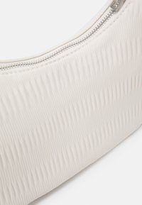 Biała torebka o fakturze z falistym wzorem, z zapięciem na zamek i srebrnymi akcentami, o gładkim wykończeniu tkaniny. Kompaktowy i zaokrąglony kształt.