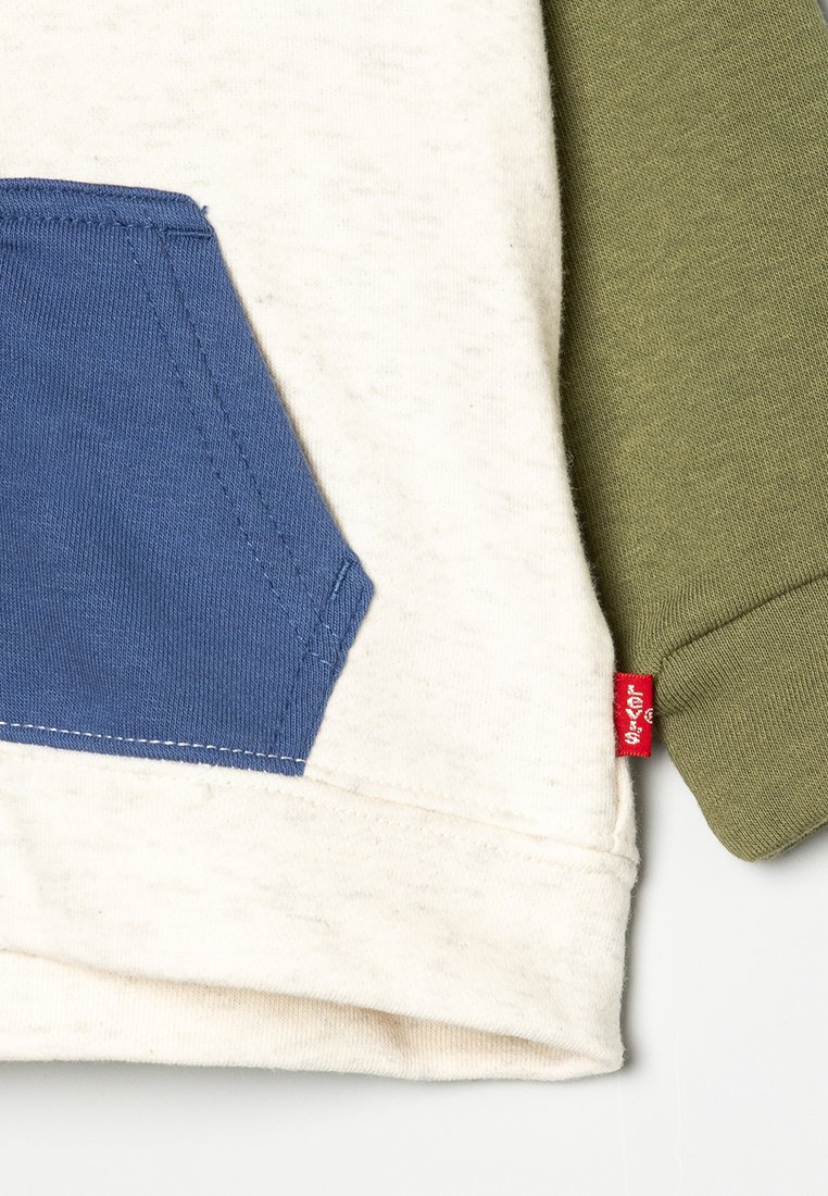 Tasca blu su tessuto crema con manica oliva e piccolo tag del brand Levi's rosso sul bordo.