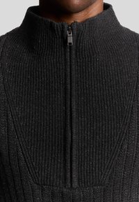 Zwarte geribde trui met hoge kraag en rits tot halverwege. De stof lijkt textuur te hebben, met een gestructureerd ontwerp en nette stiknaden.