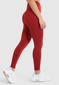Hochgeschnittene, gerippte Leggings in einem verbrannten Orangeton, aus dehnbarem Stoff gefertigt, kombiniert mit weißen Sportschuhen mit Luftpolsterung.