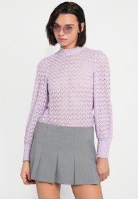 Μωβ μακρυμάνικη μπλούζα με ανάγλυφο σχέδιο ψαροκόκαλο και ψηλό λαιμό, σε συνδυασμό με γκρι μίνι φούστα με πιέτες.