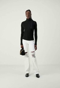 Suéter preto de gola alta canelada, jeans brancos flare com rasgos proeminentes e mules pretos de salto. Pequena bolsa preta com detalhe em corrente.