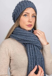 Šedá pletená čepice s ribbovanou strukturou a odpovídajícím silným šálkem. Šál má volnou, robustní pleteninu. Oba doplňky jsou měkké a pohodlné.