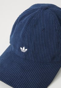 Navyblauwe corduroy pet met een witte geborduurde logo. De gestructureerde stof heeft zichtbare ribbelpatronen en een gebogen klep.