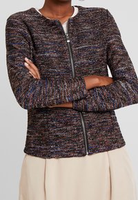 Giacca intrecciata nera e multicolore con collo rotondo, maniche lunghe e zip frontale. Tessuto testurizzato e vestibilità su misura.