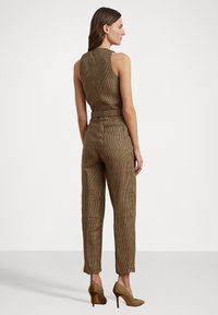 Combinaison à carreaux bruns avec une taille cintrée, un design sans manches et des jambes fuselées ; accompagnée de chaussures à talons hauts brunes.