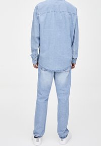 Hellblaues Jeanshemd mit langen Ärmeln und Knopfmanschetten, kombiniert mit hellblauen Jeans. Das Outfit hat einen lockeren Schnitt und eine mittlere Waschung.