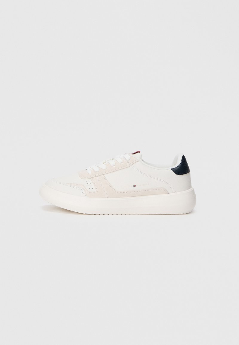 Hvid sneaker med overdel i ruskind og læder, flade snørebånd, rund tå og en kontrasterende marineblå hælkant. Tykk gummisål.
