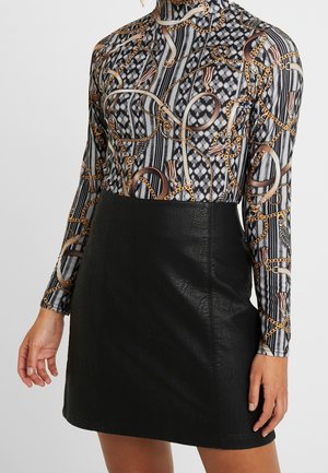 Top de cuello alto con patrón de cadenas en negro, blanco y dorado, combinado con una minifalda de cuero sintético negro de talle alto.