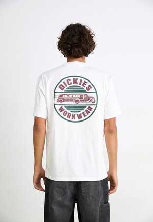 T-shirt en coton blanc avec un graphique circulaire au dos, comprenant "DICKIES" et une illustration d'un camion, accentuée de vert et de marron.