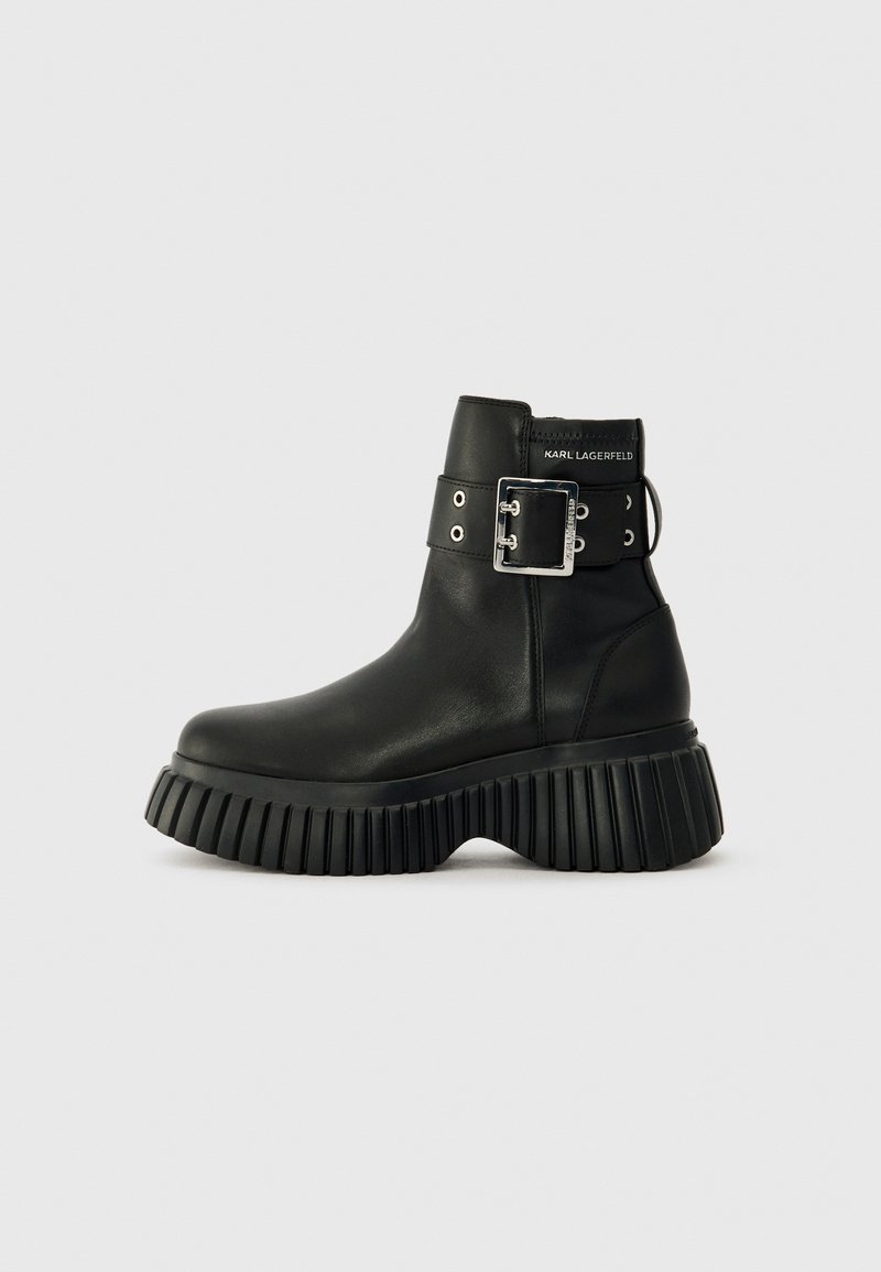 Black leather ankle boots with a thick ribbed sole. Features a wide ankle strap with a silver buckle and eyelets. Minimal branding at the back.