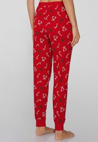 Rode pyjamabroek van katoen, met witte zuurstok- en groene hulstprints, tapered leg ontwerp met rib ribbels bij de enkels.