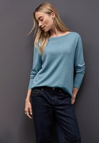 Maglione azzurro chiaro con maniche lunghe e scollatura ampia, abbinato a jeans in denim scuro. Tessuto morbido e vestibilità casual.