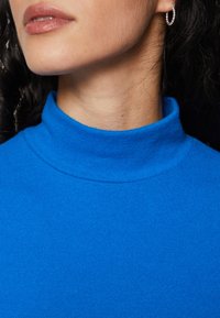 Pulover tricotat bleu cu guler înalt, cu un guler strâns și o textură netedă, evidențiind o culoare vibrantă și un design minimal.