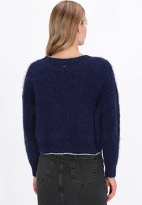Navyblauwe fuzzy trui met een cropped ontwerp, losse pasvorm en geribde boord. Heeft een ronde halslijn en iets verlaagde schouders.