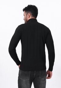 Suéter negro de punto con textura de canalé, rayas verticales y cuello alto. Combinado con jeans gris oscuro de corte casual.