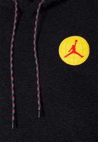 Schwarzer Fleece-Hoodie mit einem gelben runden Logo und einer roten Silhouette sowie mehrfarbigen geflochtenen Kordeln mit Kunststoffspitzen.